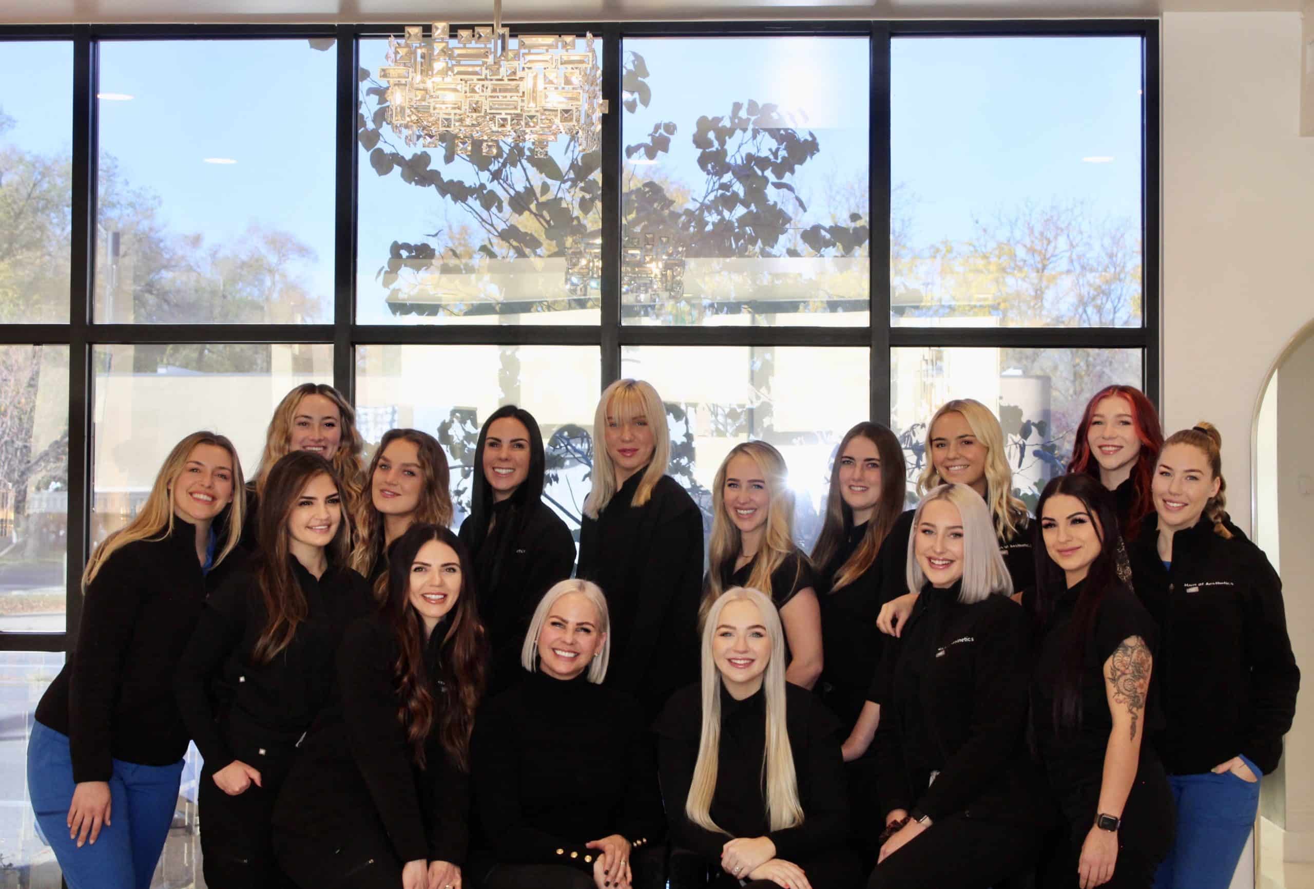 Haus of aesthetics team standing together smiling in front of a large window inside the beautiful med spa in Salt Lake City. Career opportunities for anyone in the Aesthetics industry.
